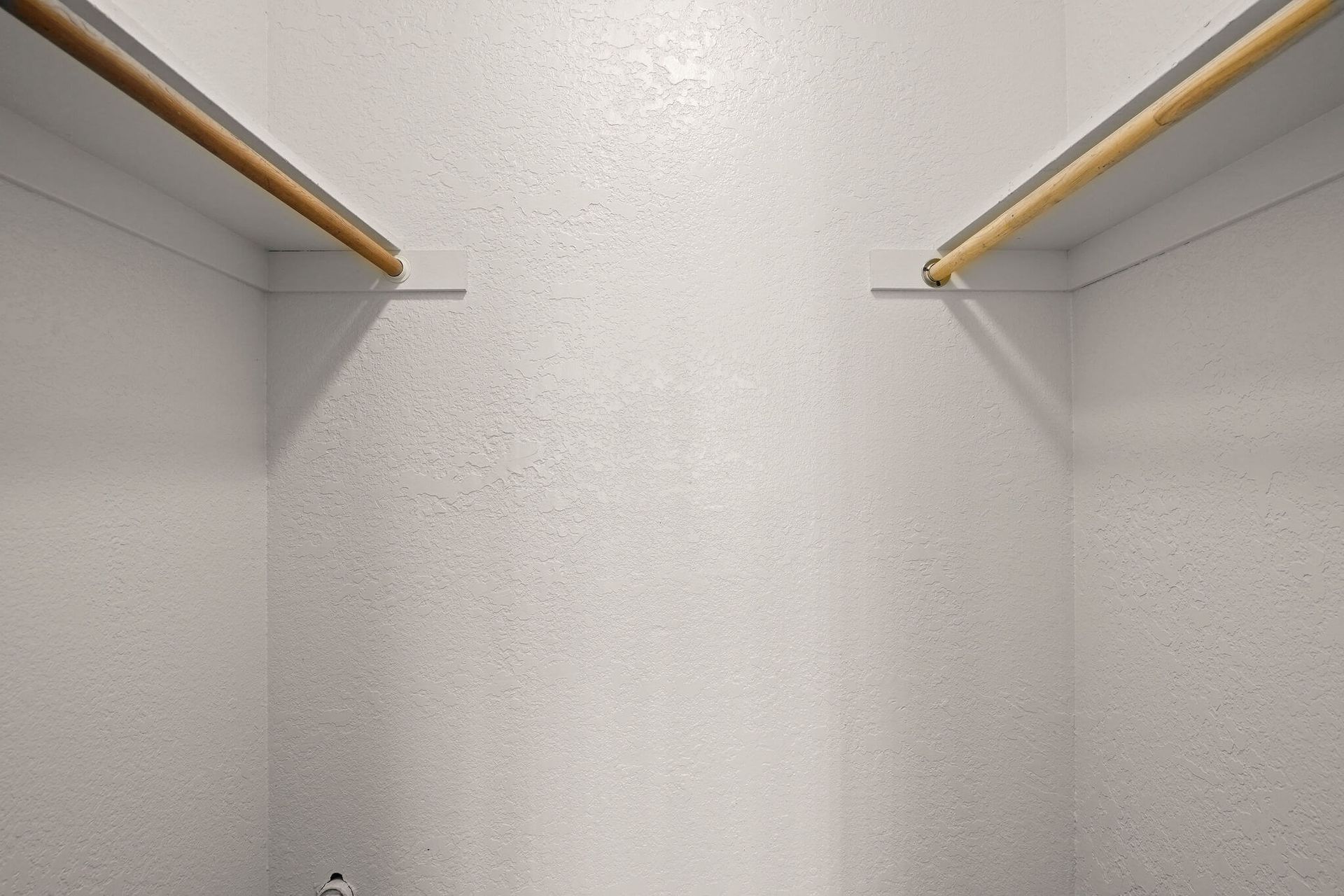 Empty white closet with wooden hanging rods on both sides and a centered back wall.