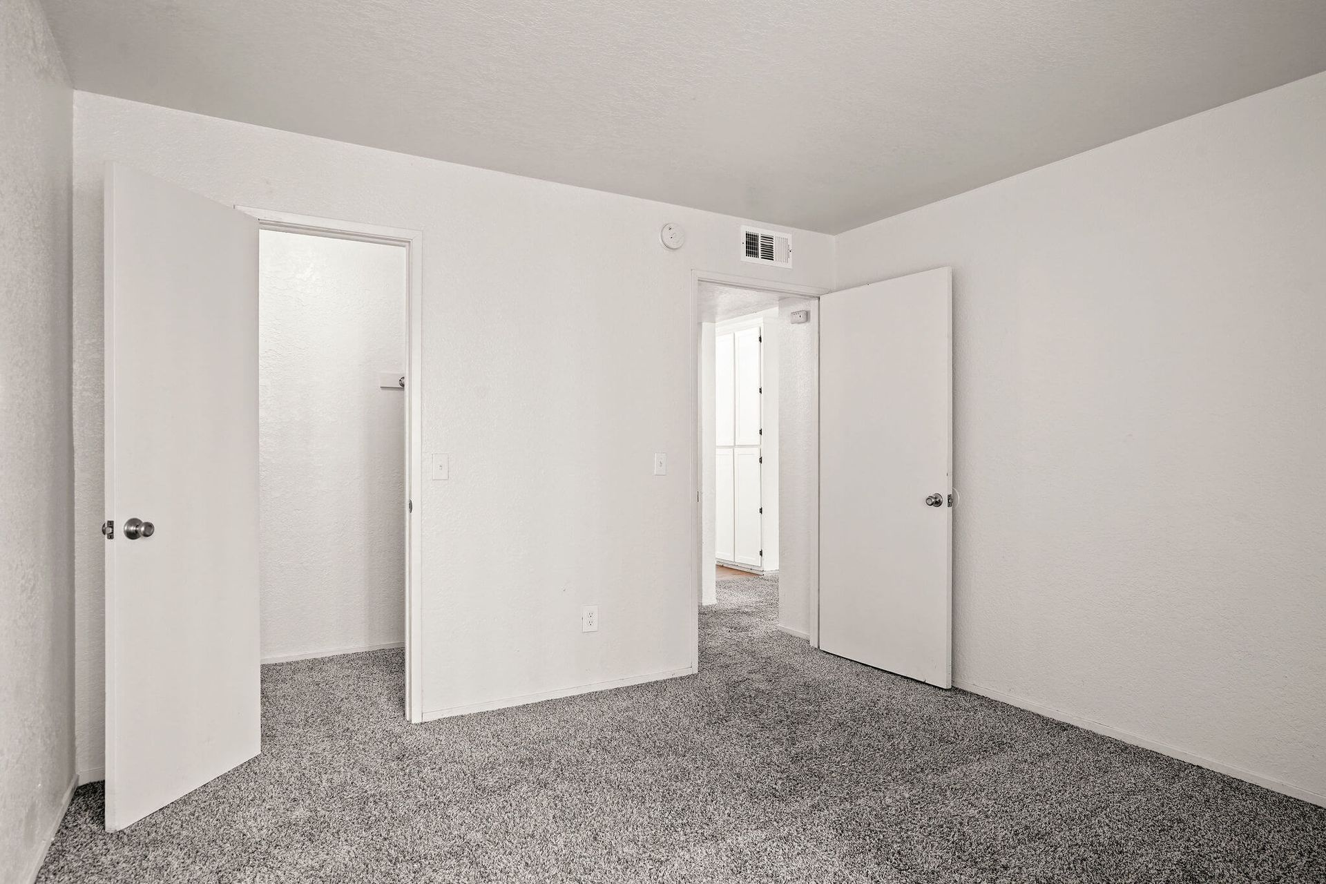 Empty carpeted bedroom with white walls and open closet doors