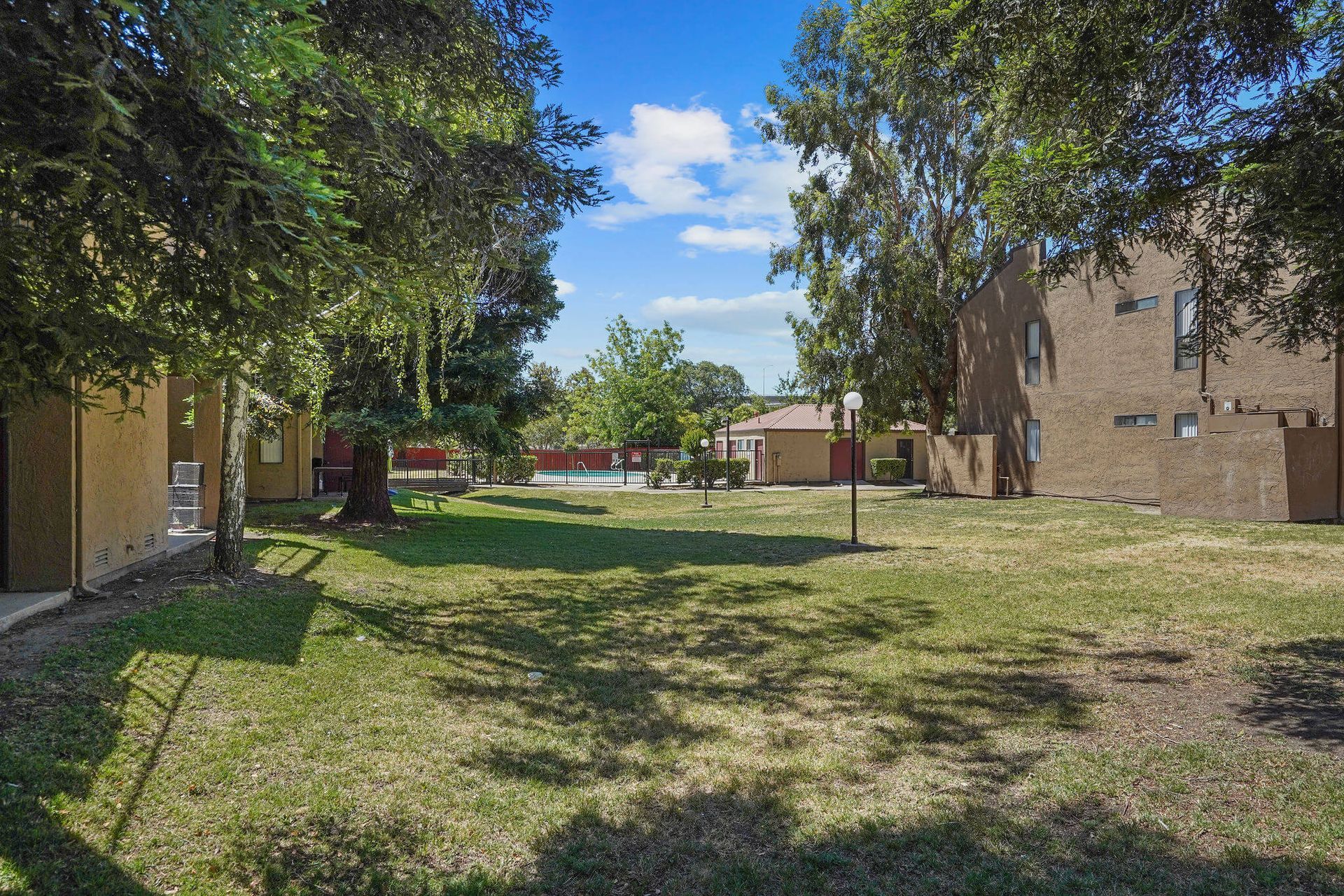 Grassy courtyard between apartment buildings under a blue sky, with trees and a picnic table in the distance