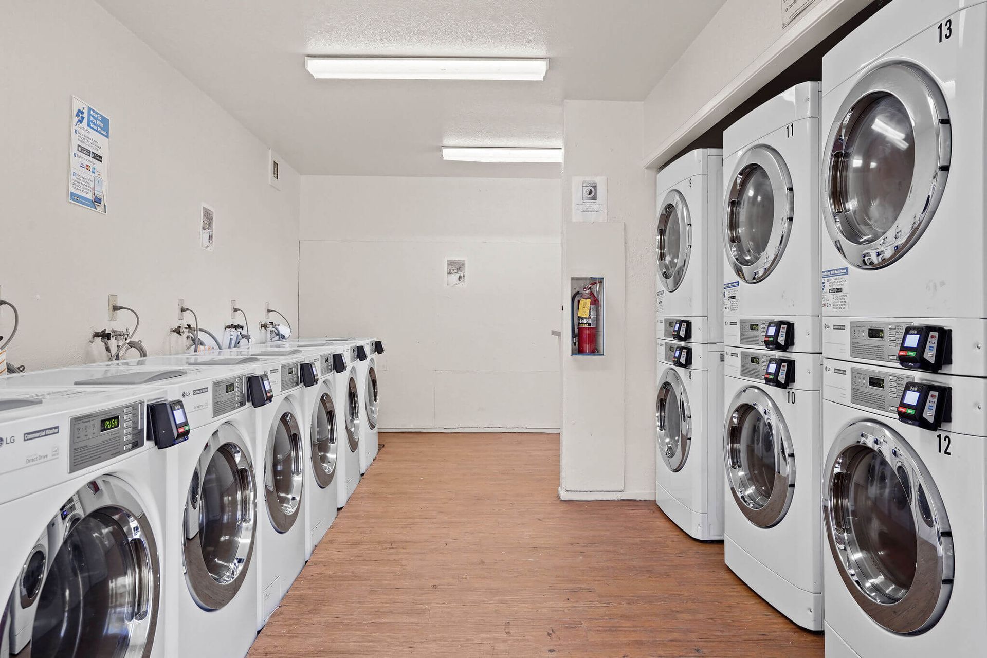 Bright laundromat with rows of white washers and dryers along both walls.