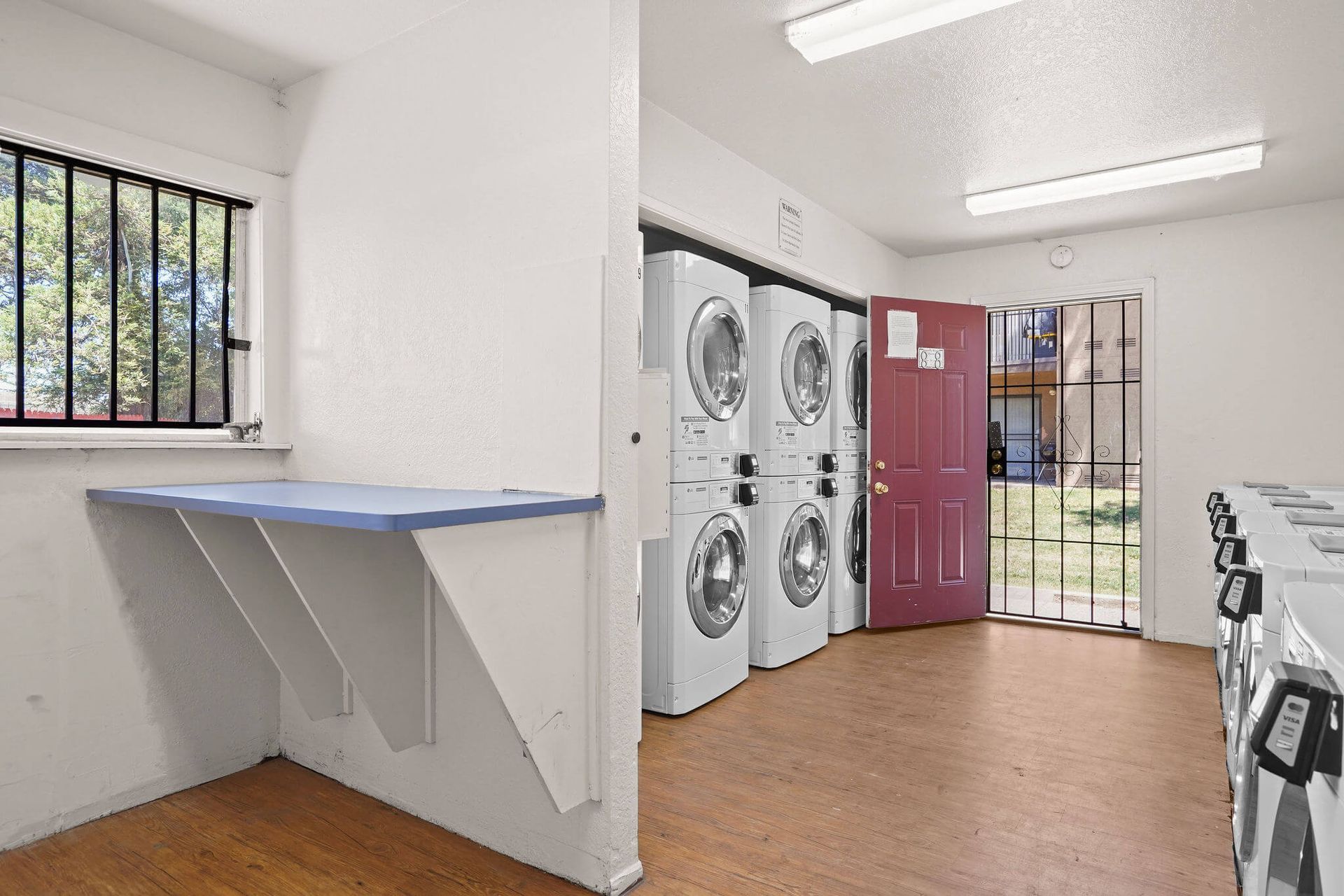 Laundry room with stacked washers, red door, barred window, and folding counter on the left