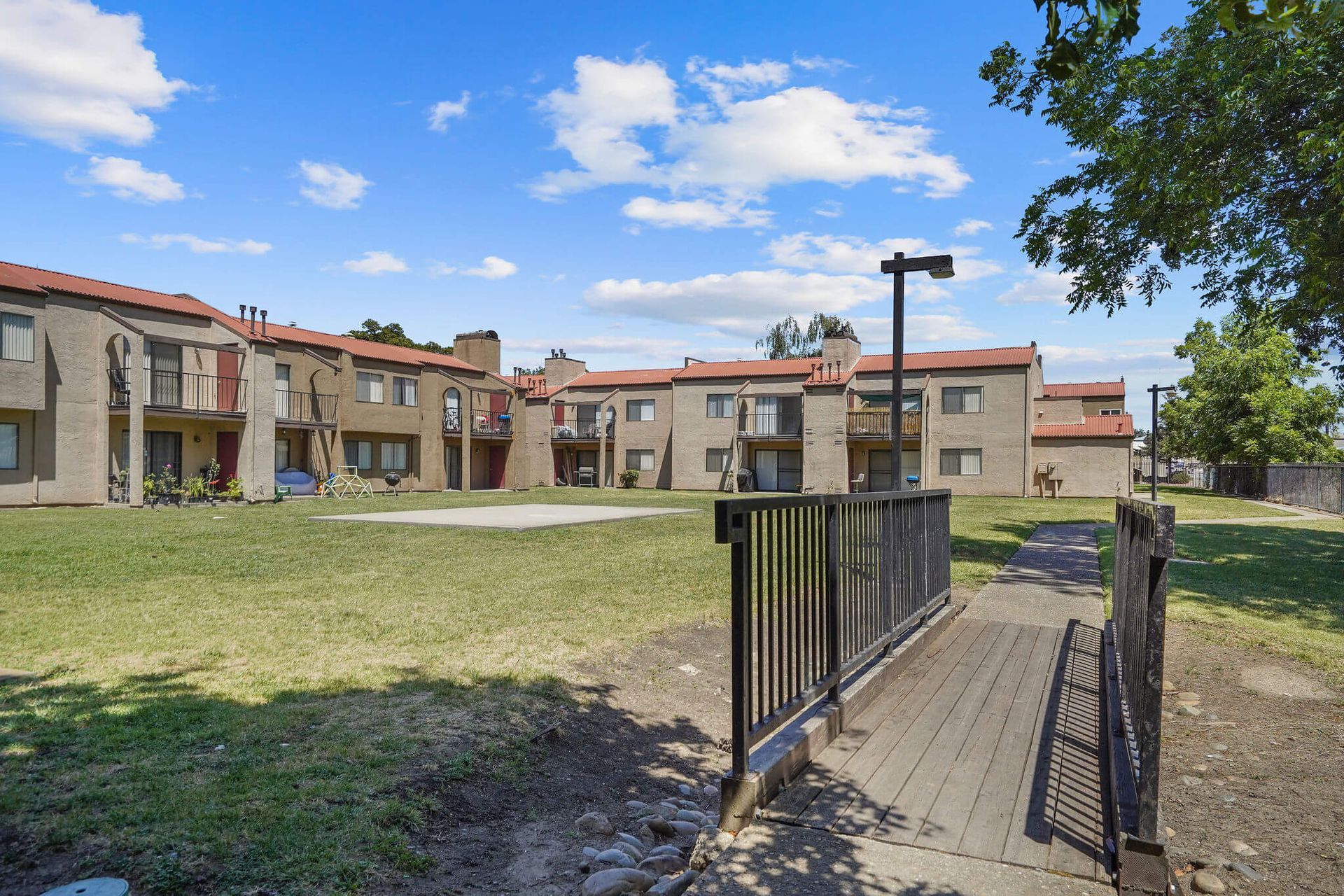 Apartment complex courtyard with grass, walkway, and metal railing under a blue sky
