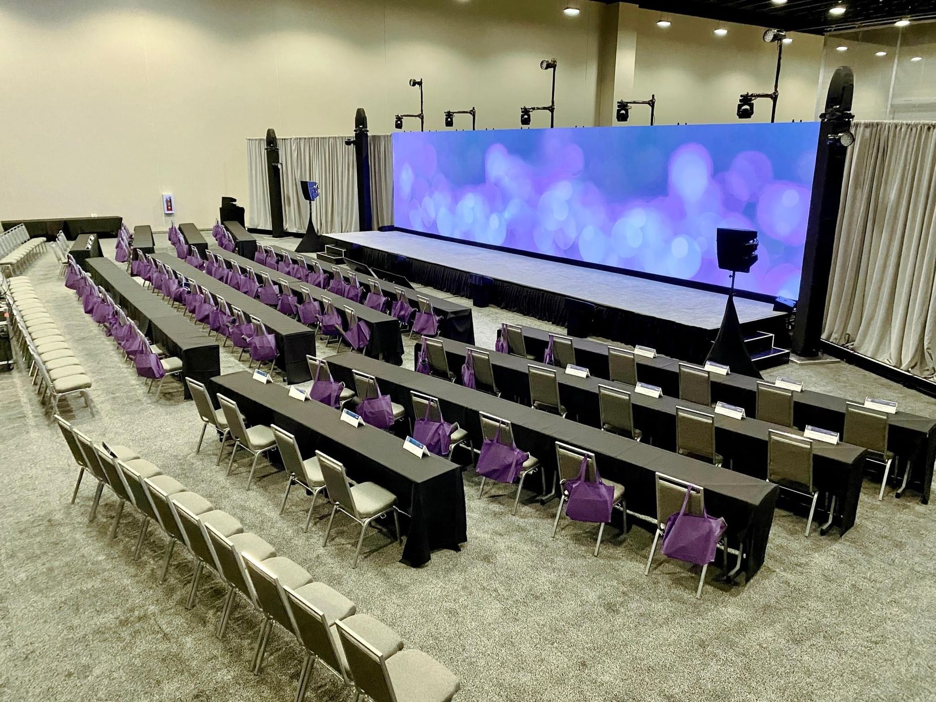 A large conference room with long tables and chairs and a stage.
