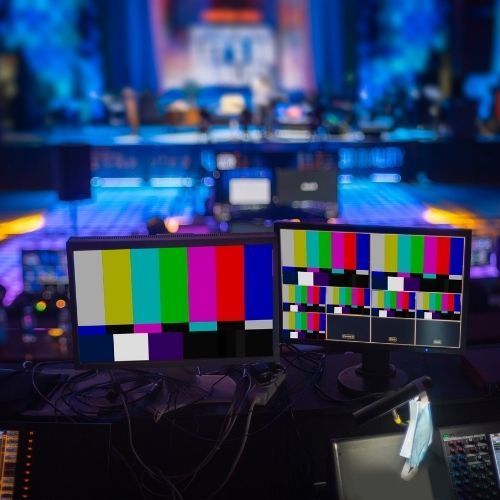 Two monitors are sitting on a table in front of a stage. Event production. AV set up. 