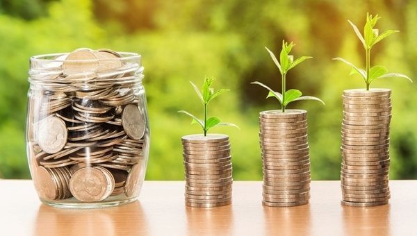 A jar filled with coins and three stacks of coins with plants growing out of them. Maximizing savings. 