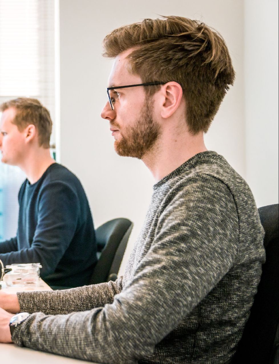 A man with glasses is sitting at a desk with another man