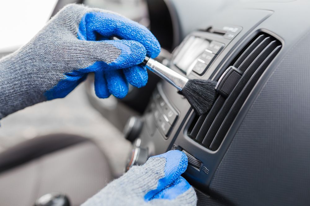Gloved Hands Cleaning a Car Dashboard Air Vent With a Brush and Cloth — Wingham Mechanical in Wingham, NSW