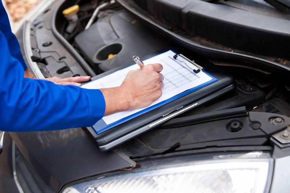 Mechanic Writing on A Clipboard Beside an Open Car Hood — Wingham Mechanical in Wingham, NSW