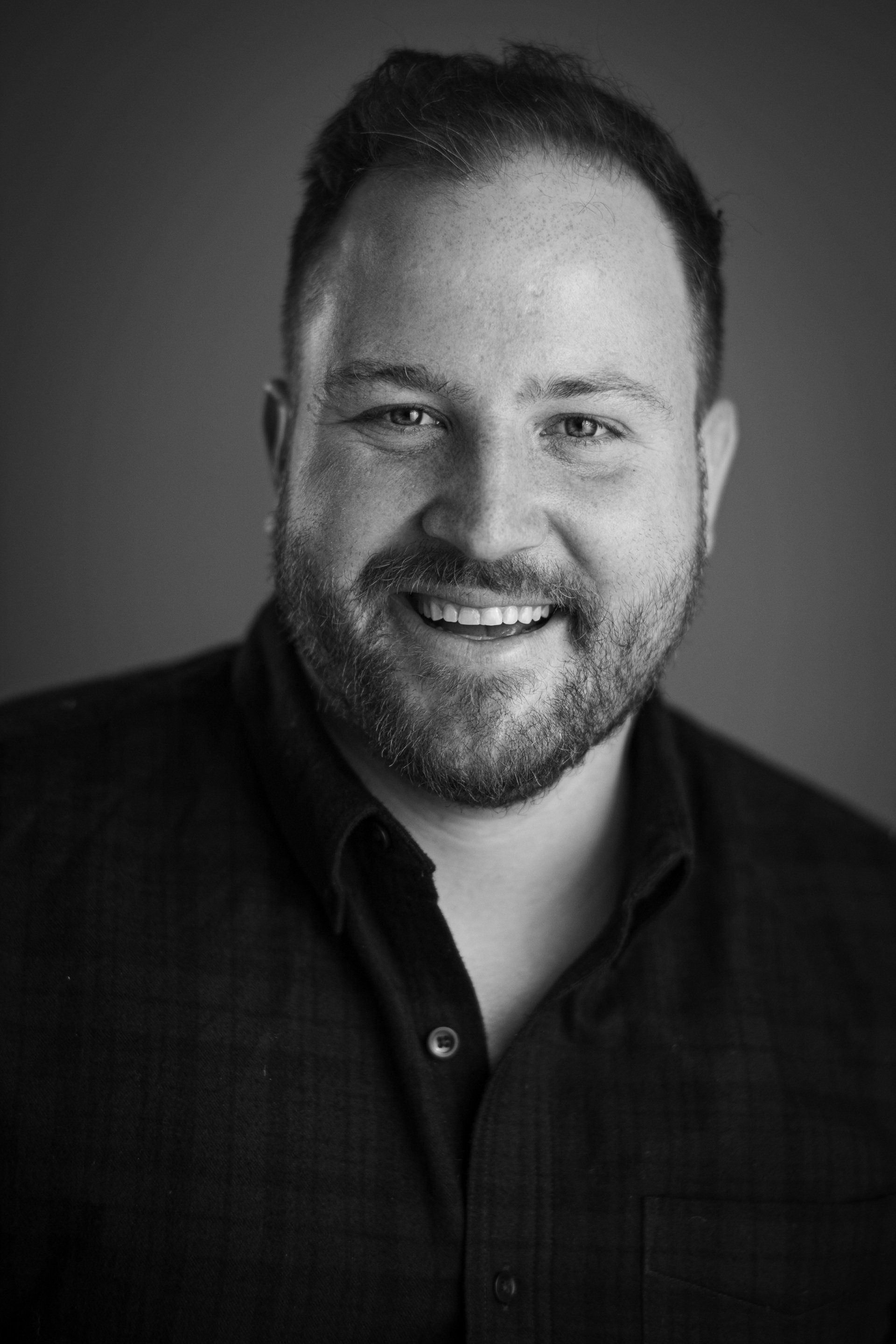 A man with a beard is smiling in a black and white photo.