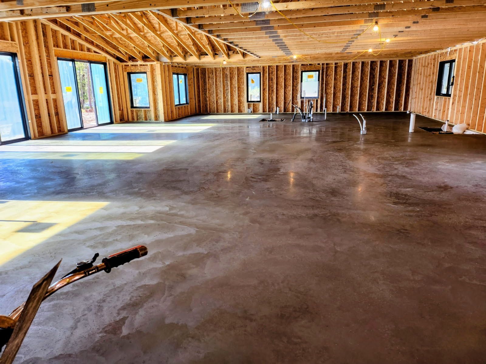 A person wearing work gloves uses a drill to fasten a metal plate to a concrete panel wall at a construction site.
