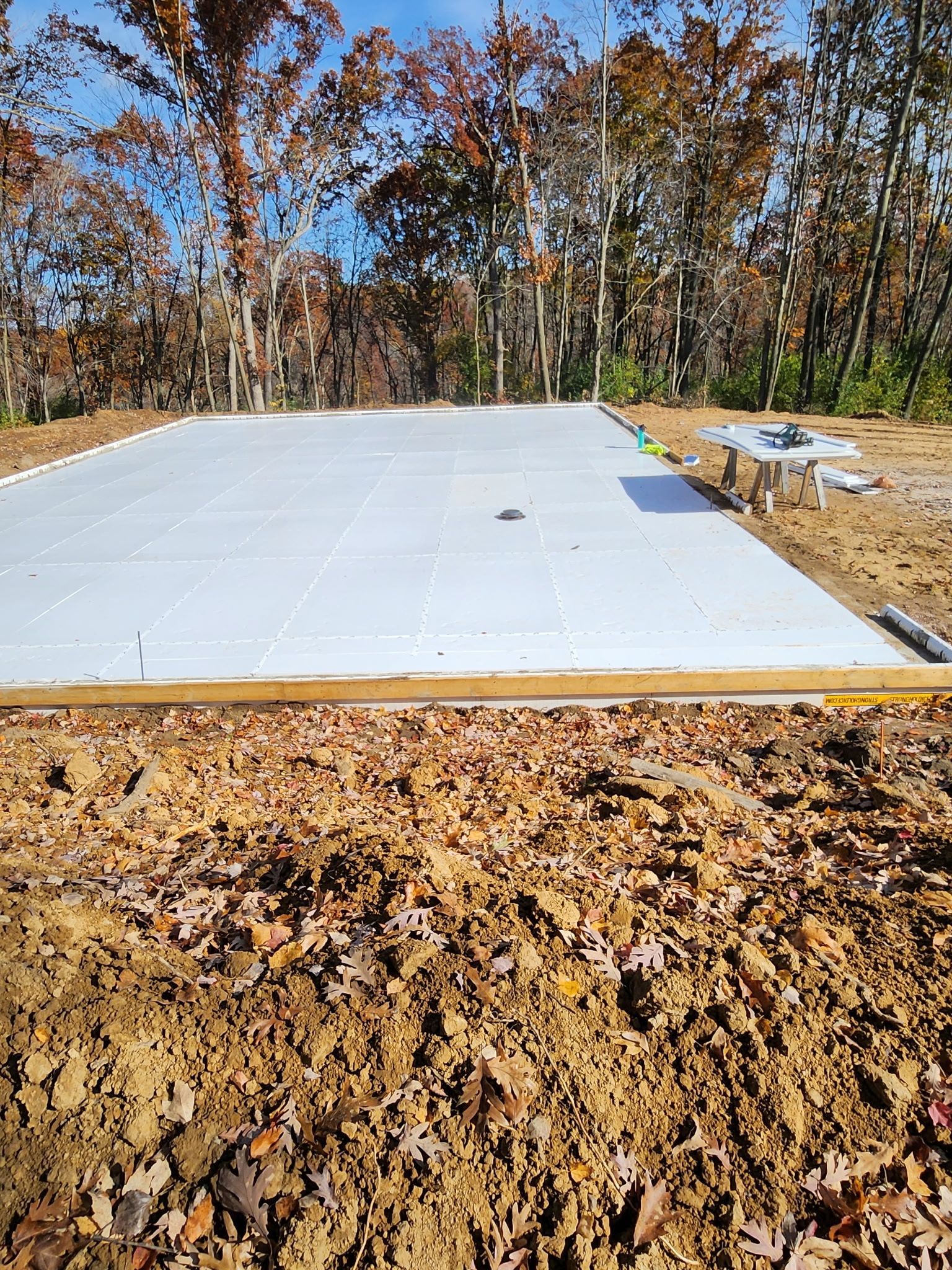 Three construction workers in hard hats and winter gear install white foam blocks on a snowy job site near a frozen lake.