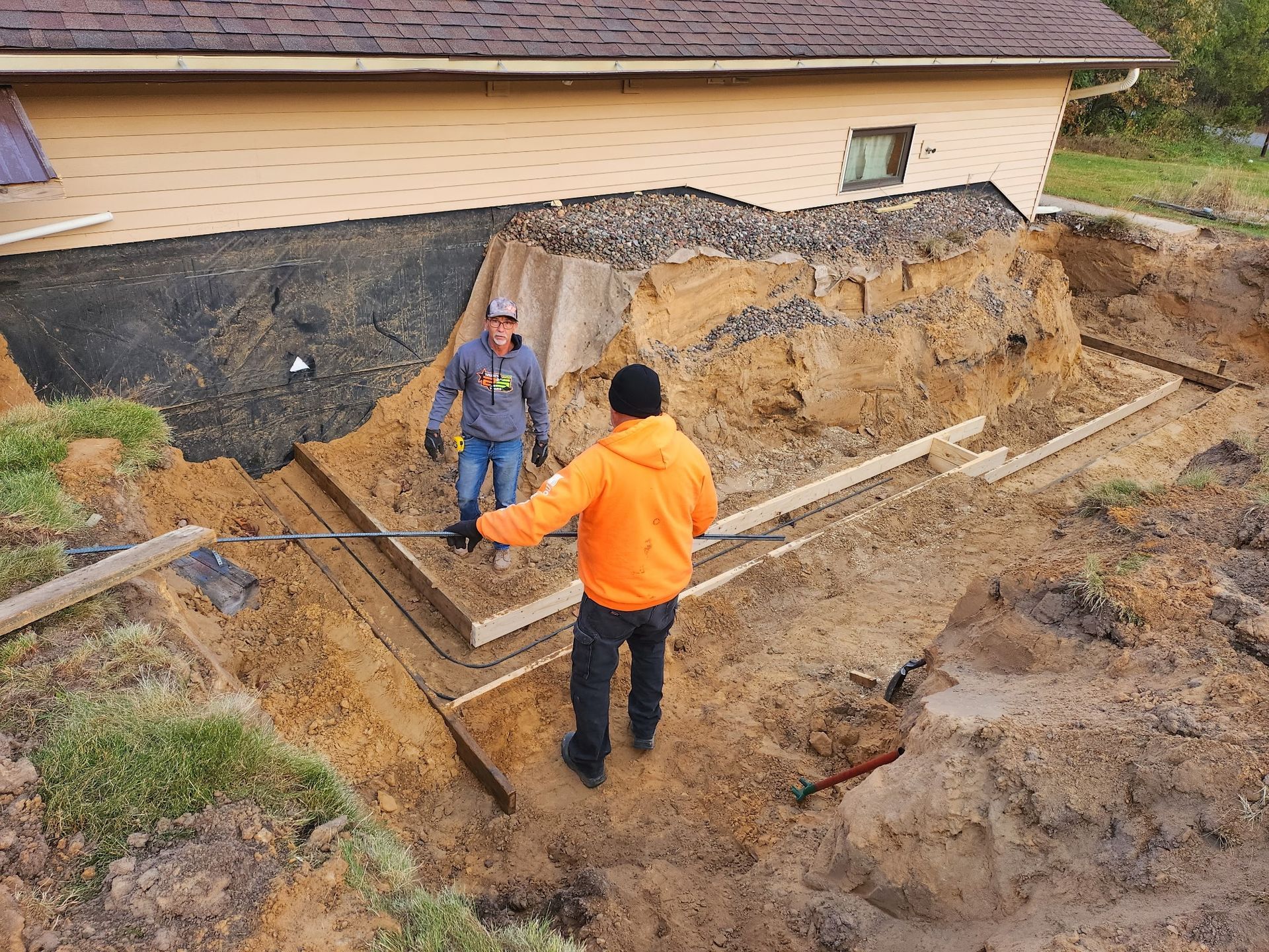 Four construction workers in safety vests and yellow hard hats pour and level wet concrete into a wooden frame.
