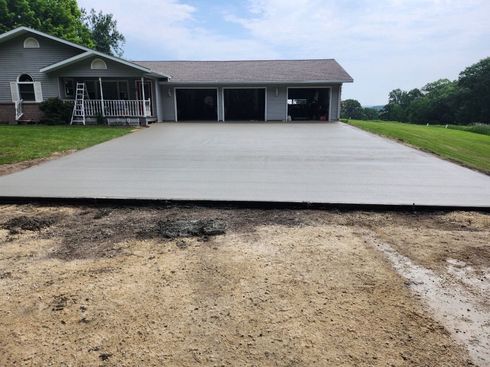 Large concrete driveway leading to a single-story house with a front porch and garage.