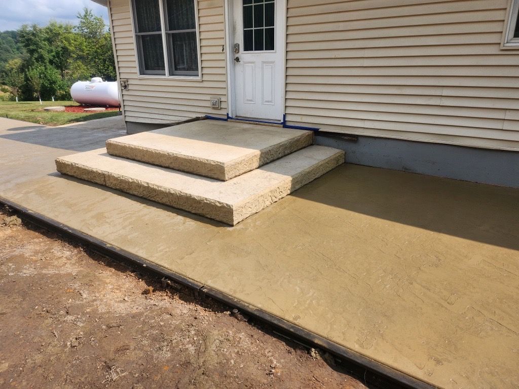 A freshly poured, smooth gray concrete slab at a construction site with wooden framing in the background.