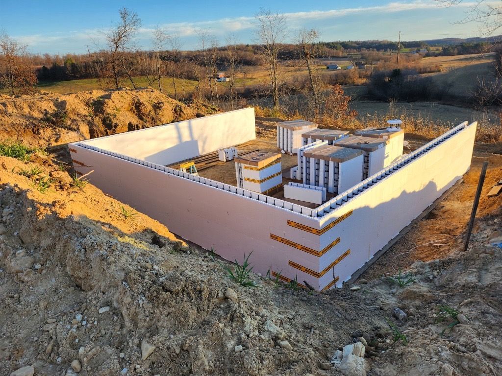 Two yellow excavators parked on a dirt construction site with a concrete foundation in the background under a blue sky.