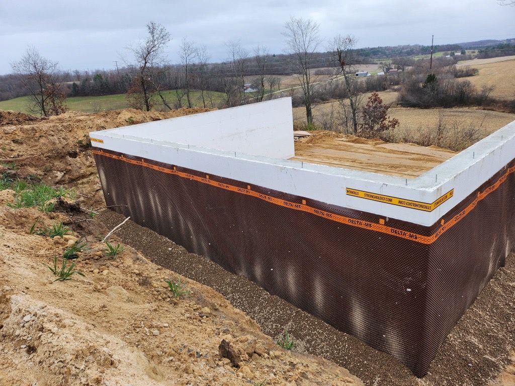 A metal skid steer bucket sits on dirt, filled with a pile of brown soil in an outdoor setting.