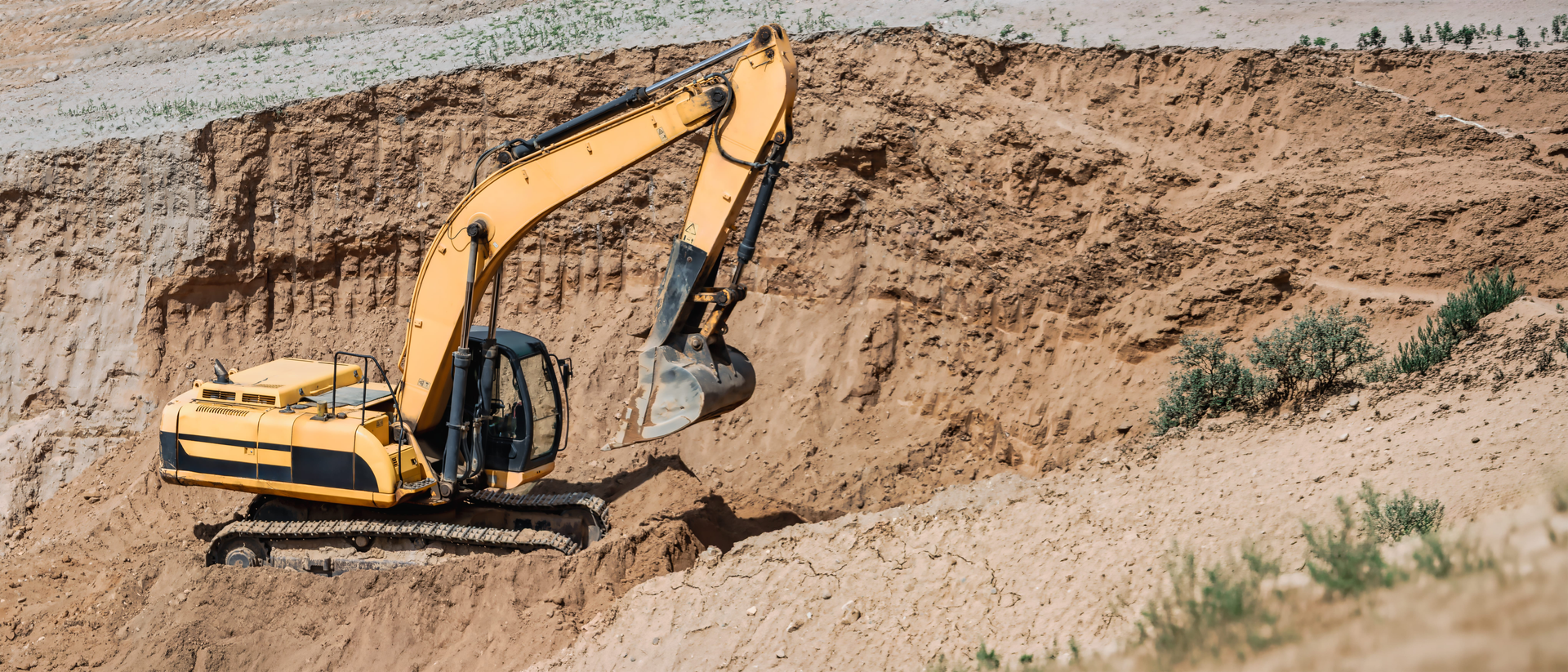 Yellow excavator digging into a sandy hillside at a construction site