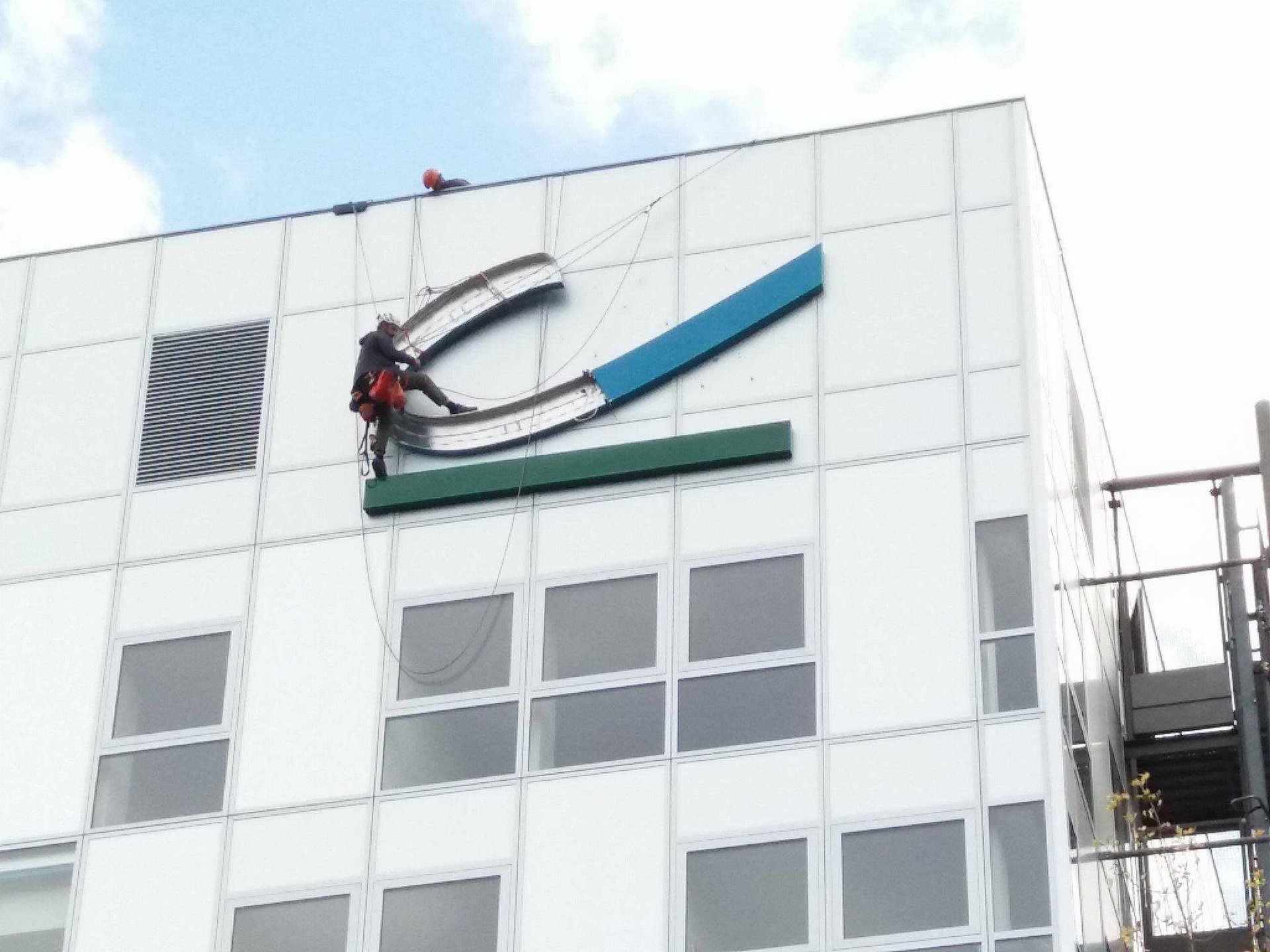 Un homme grimpe sur le côté d'un bâtiment pour retirer un panneau