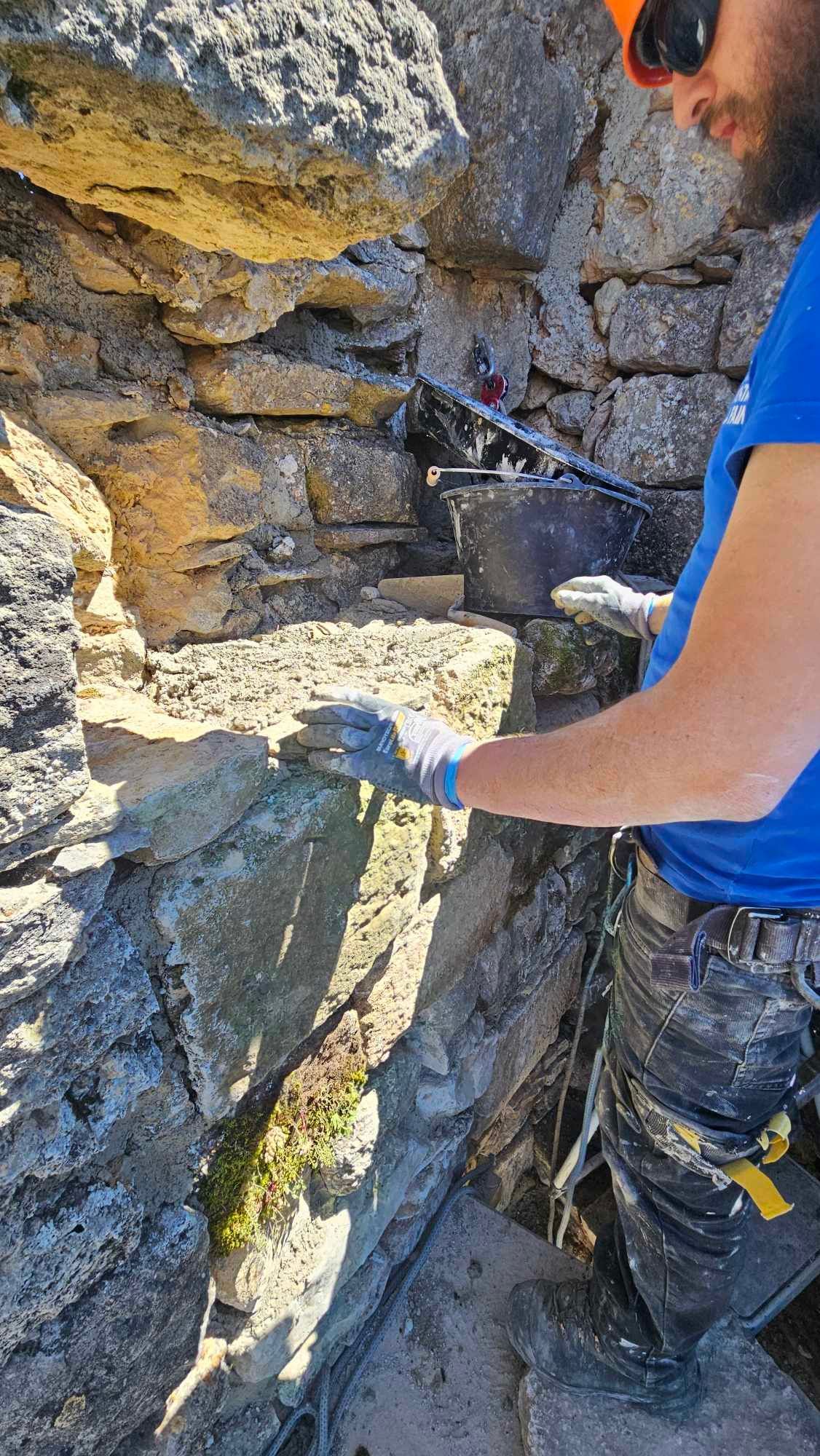 Un homme travaille sur un mur de pierre avec une tronçonneuse.