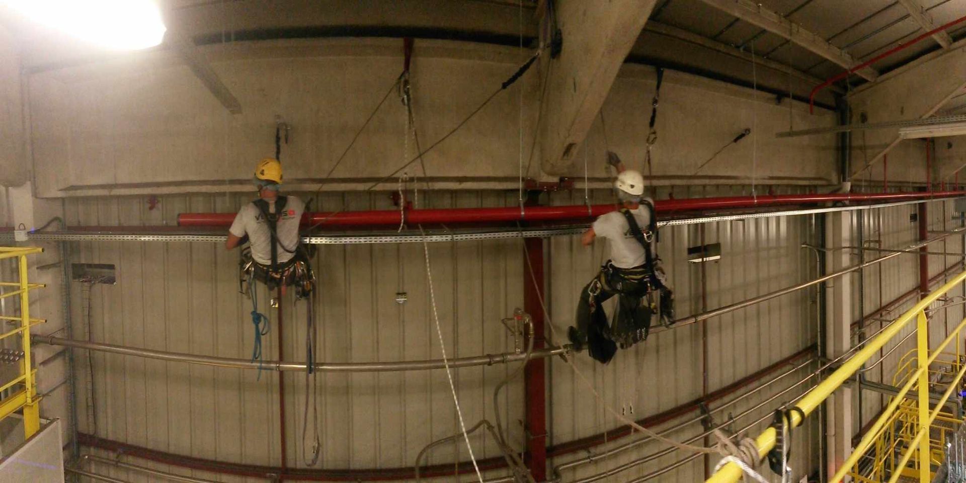 Deux hommes travaillent sur un tuyau dans un bâtiment.