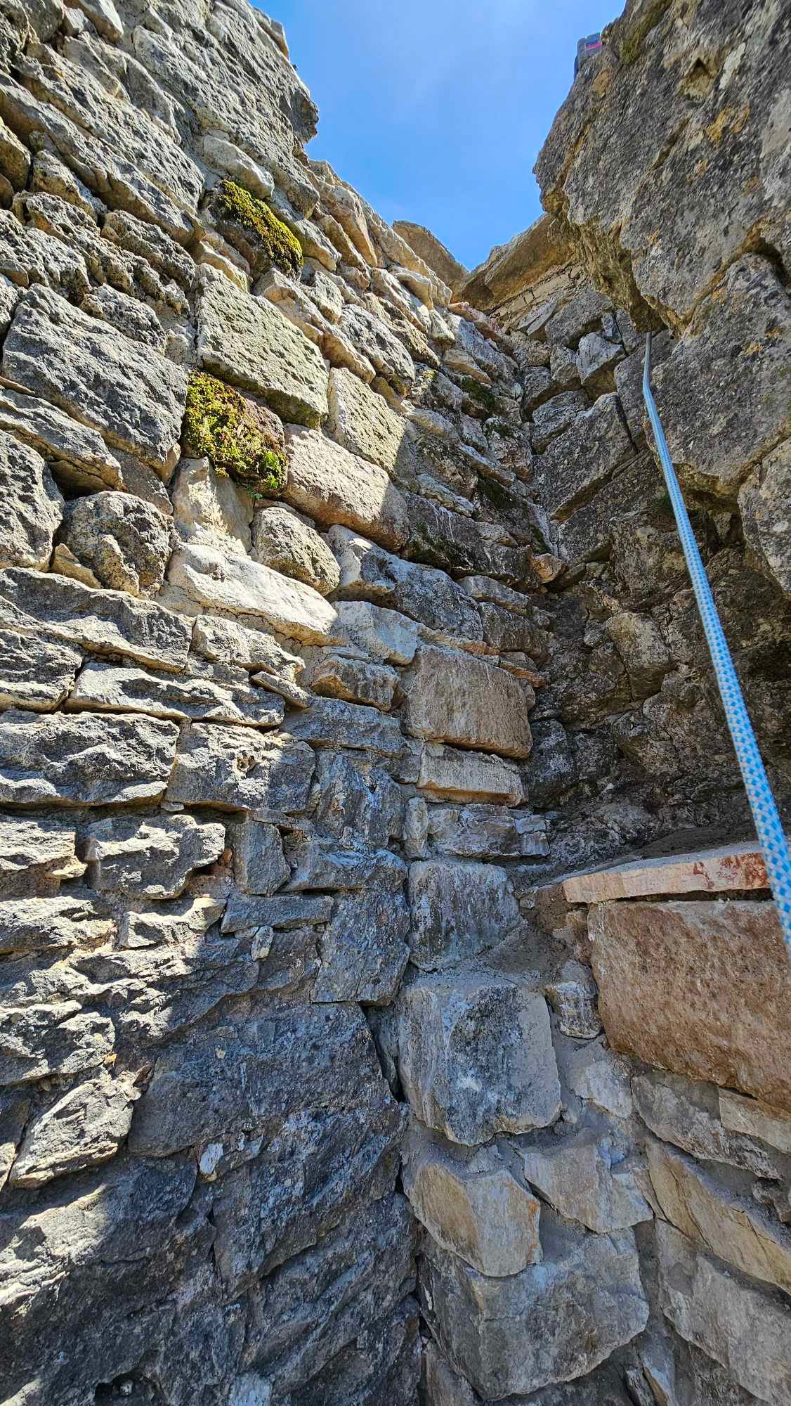 Une personne grimpe sur un mur de pierre avec une corde.