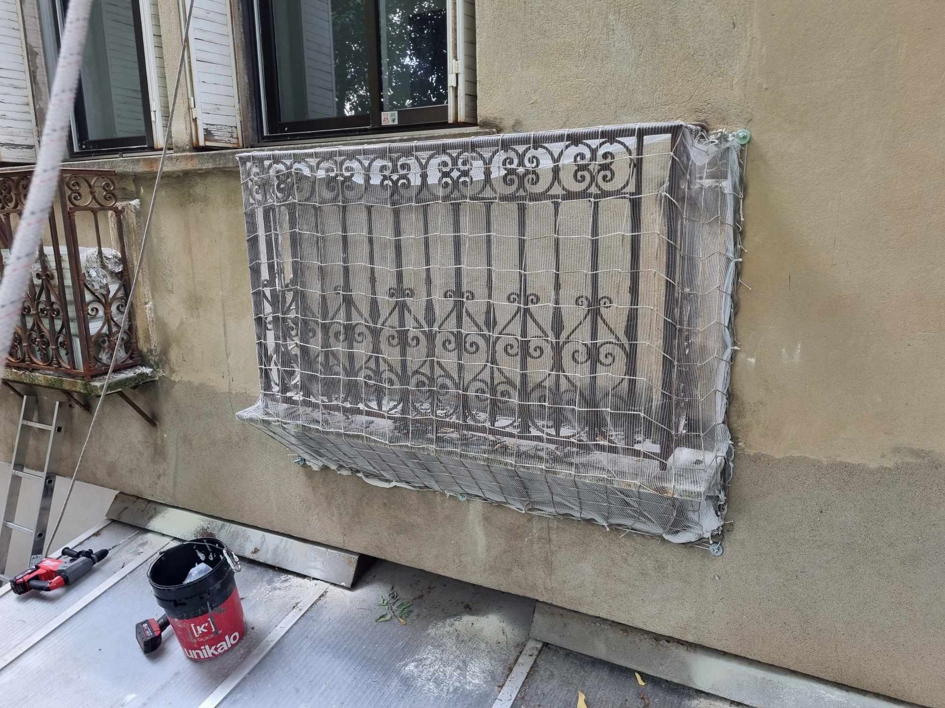 Une fenêtre avec une balustrade en fer forgé est en train d'être peinte sur le côté d'un bâtiment.