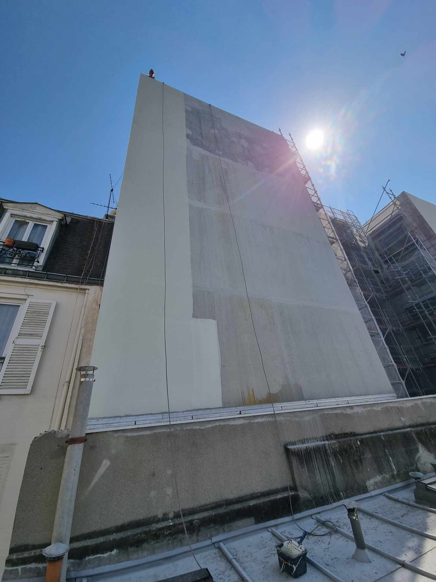 Un grand bâtiment avec un échafaudage sur le côté est en train d'être peint en blanc.