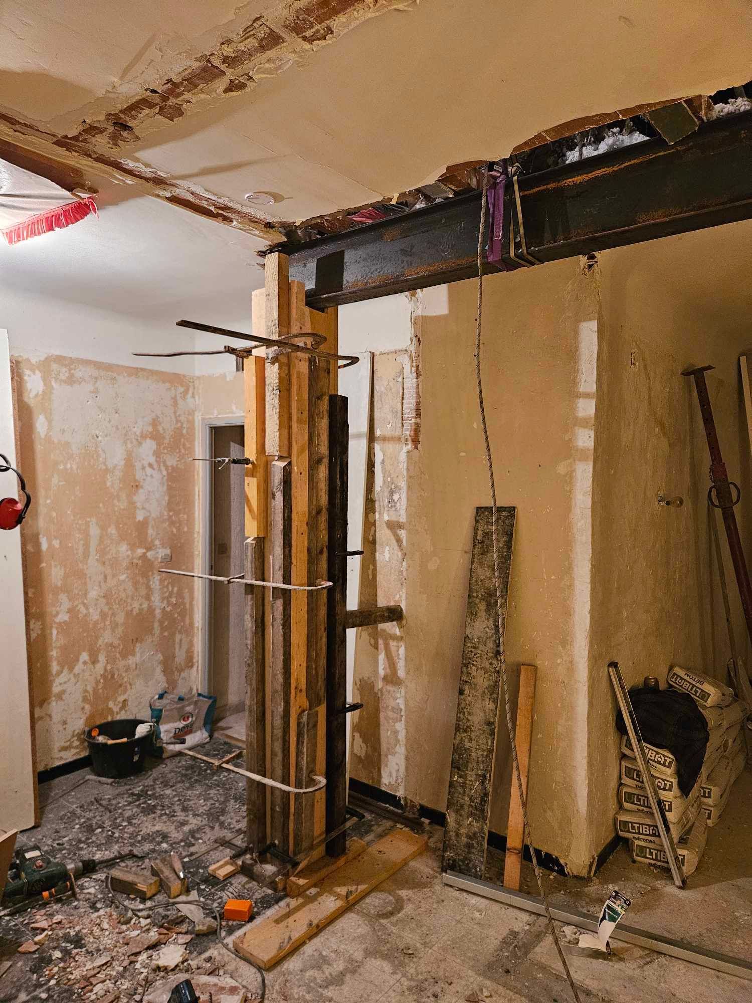 Une pièce est en cours de rénovation avec une grande poutre métallique suspendue au plafond.