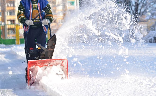 Una persona spalava la neve con una spazzaneve rossa su una strada innevata, spruzzando la neve di lato.
