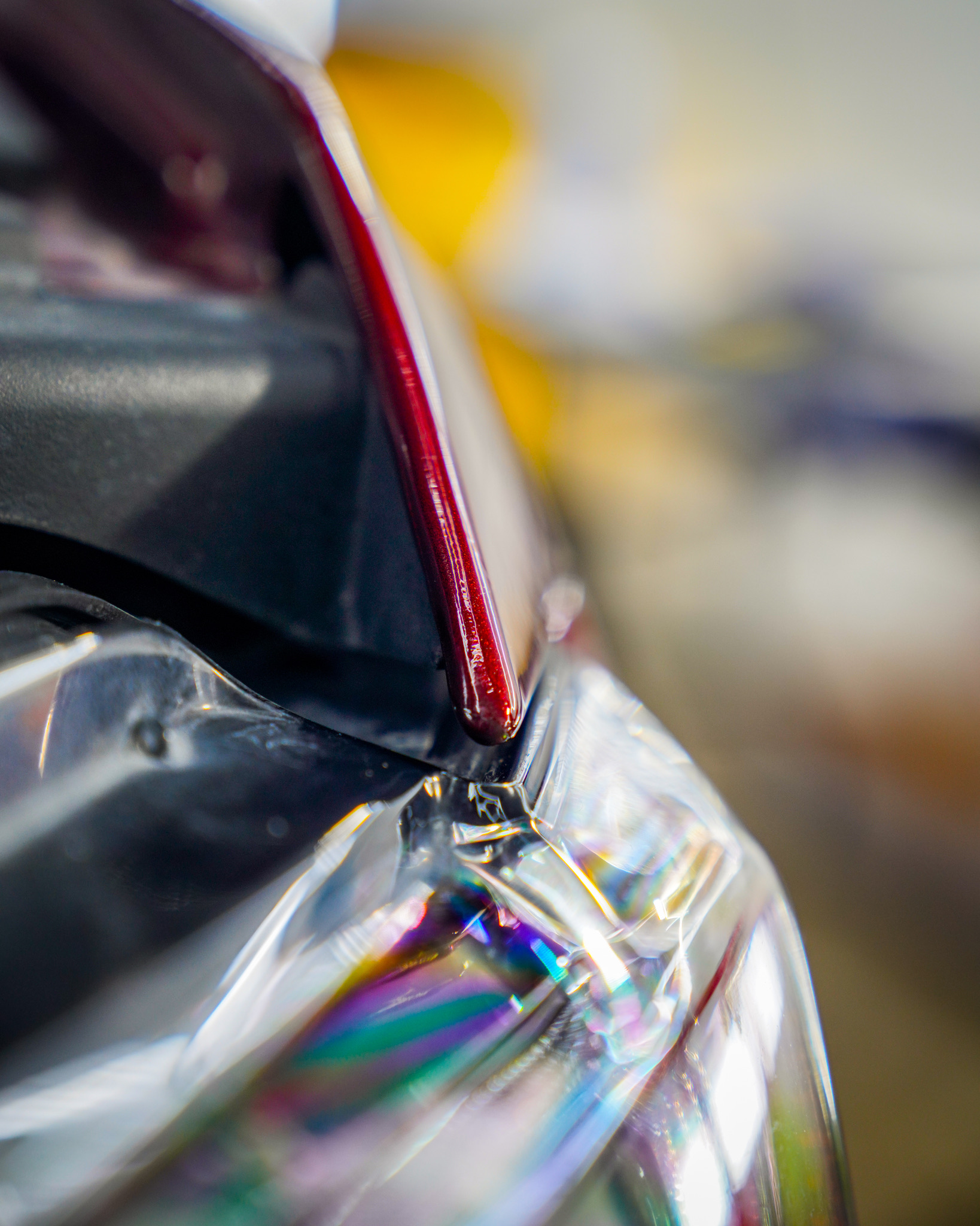 A close-up of a car's headlamp assembly, showing the sharp angle where the red painted frame meets the clear lens.