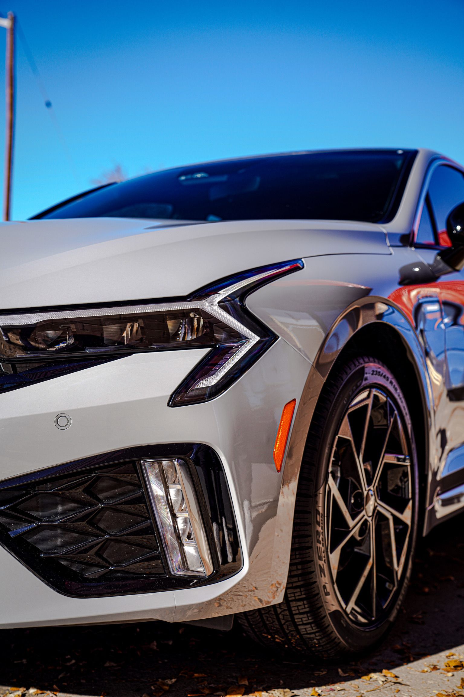 A close-up view of the front passenger side of a silver sedan featuring angular LED headlights and sporty alloy wheels.