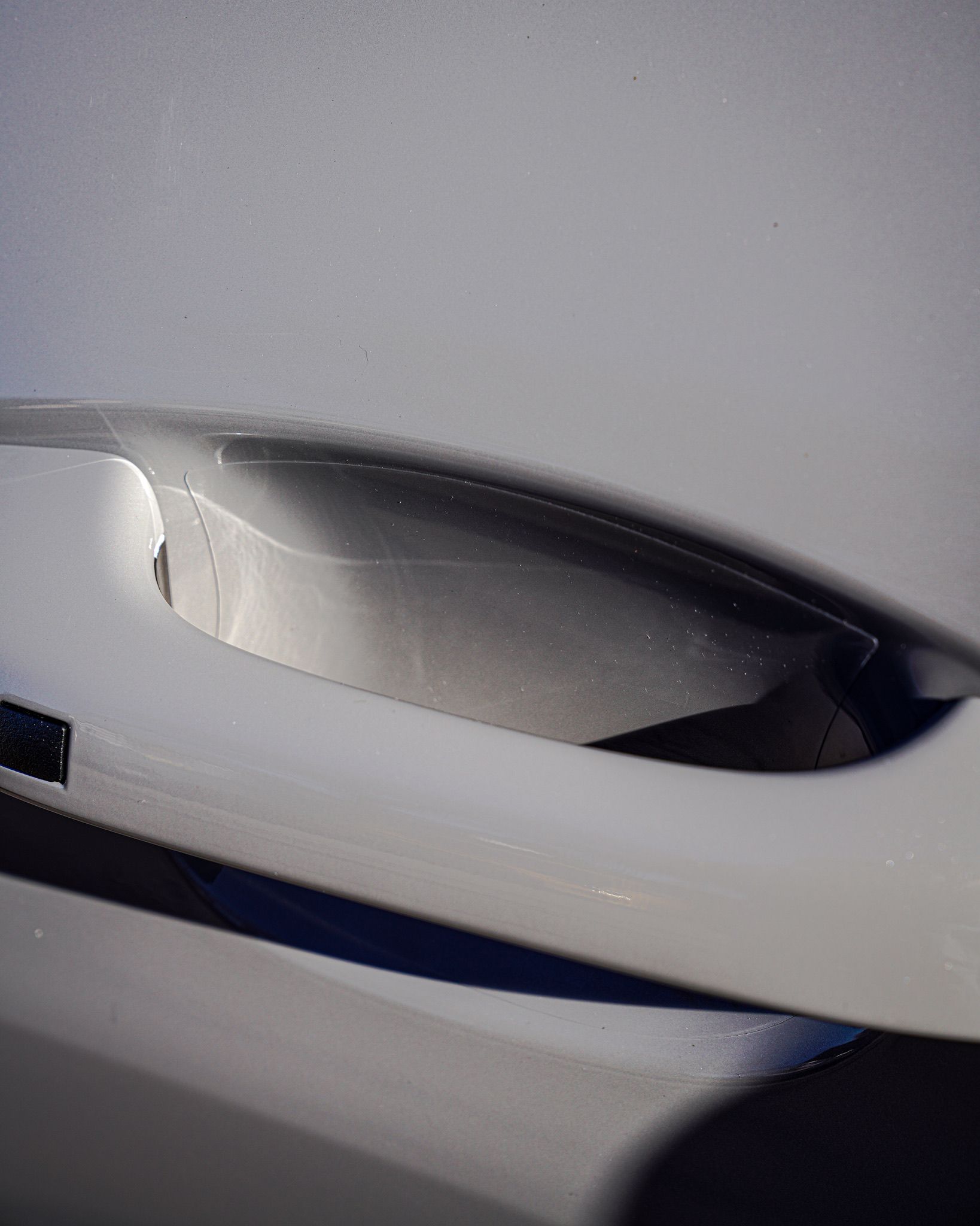 A close-up view of a white car door handle recessed into the body of the vehicle.