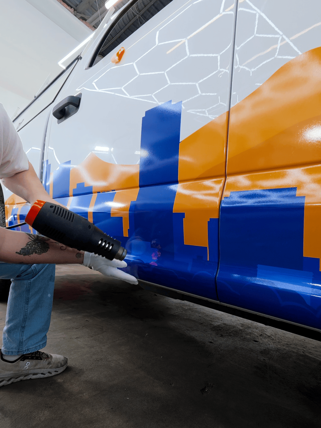 Person painting a white and orange vehicle with a blue spray gun near the lower side panel