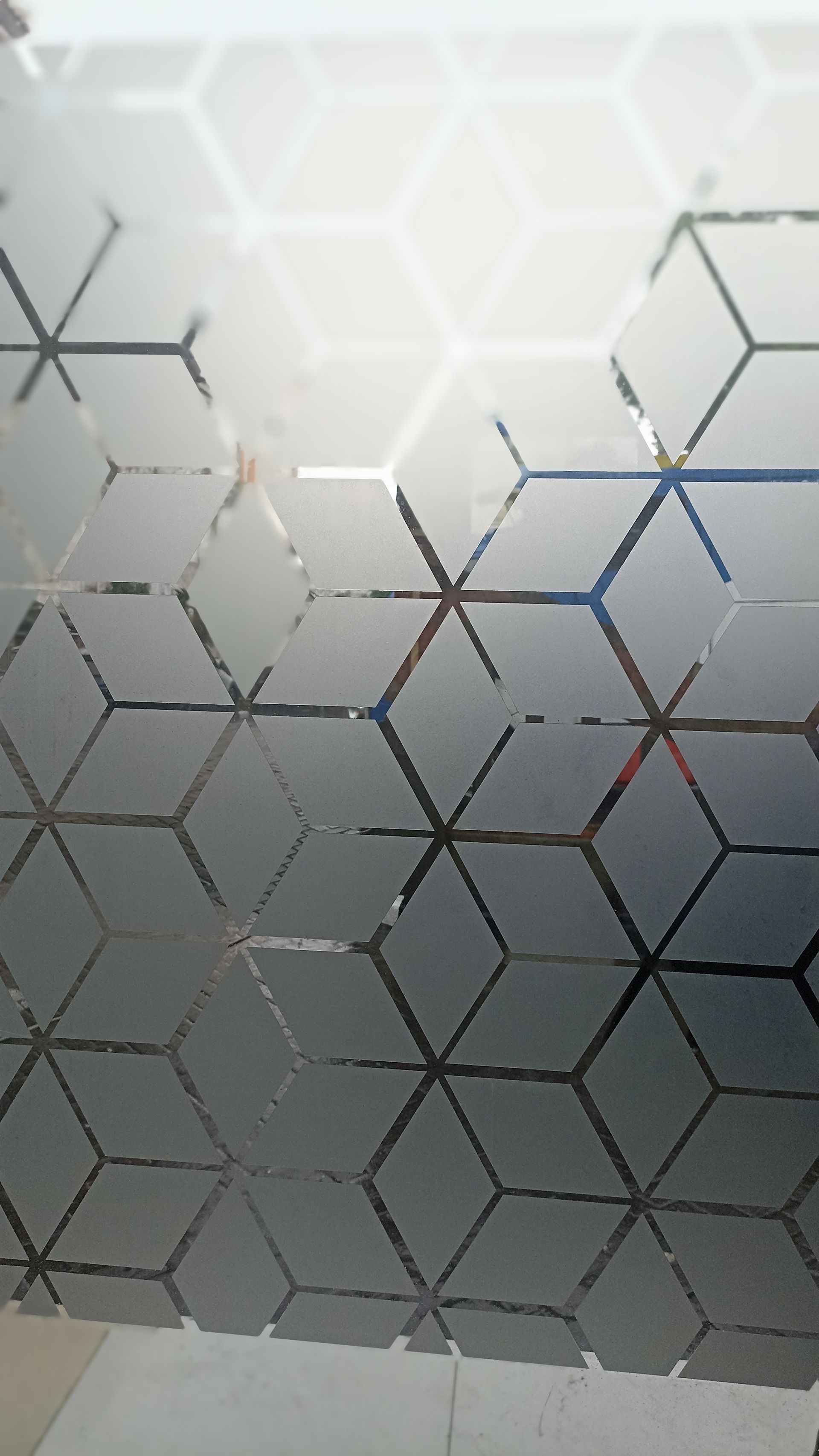 A person kneels to apply a protective film to the front bumper of a blue sports car in an auto shop.