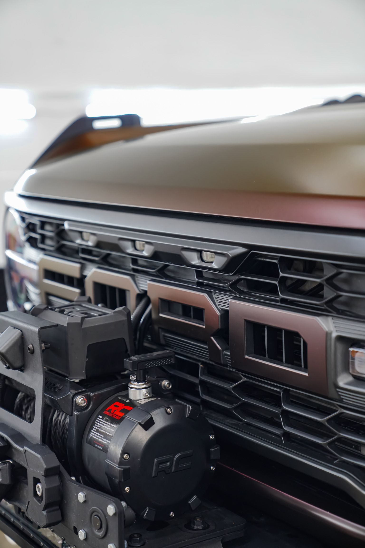 Close-up of a bronze vehicle front grille and bumper with a prominent black winch installed.