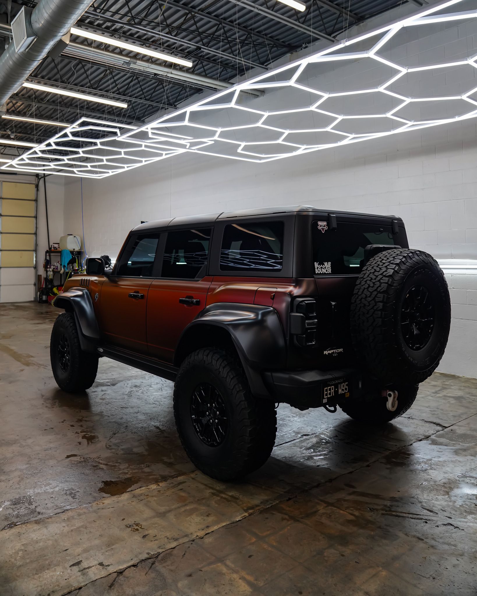 A metallic copper Ford Bronco with off-road tires and wide fender flares parked inside a garage with geometric lighting.
