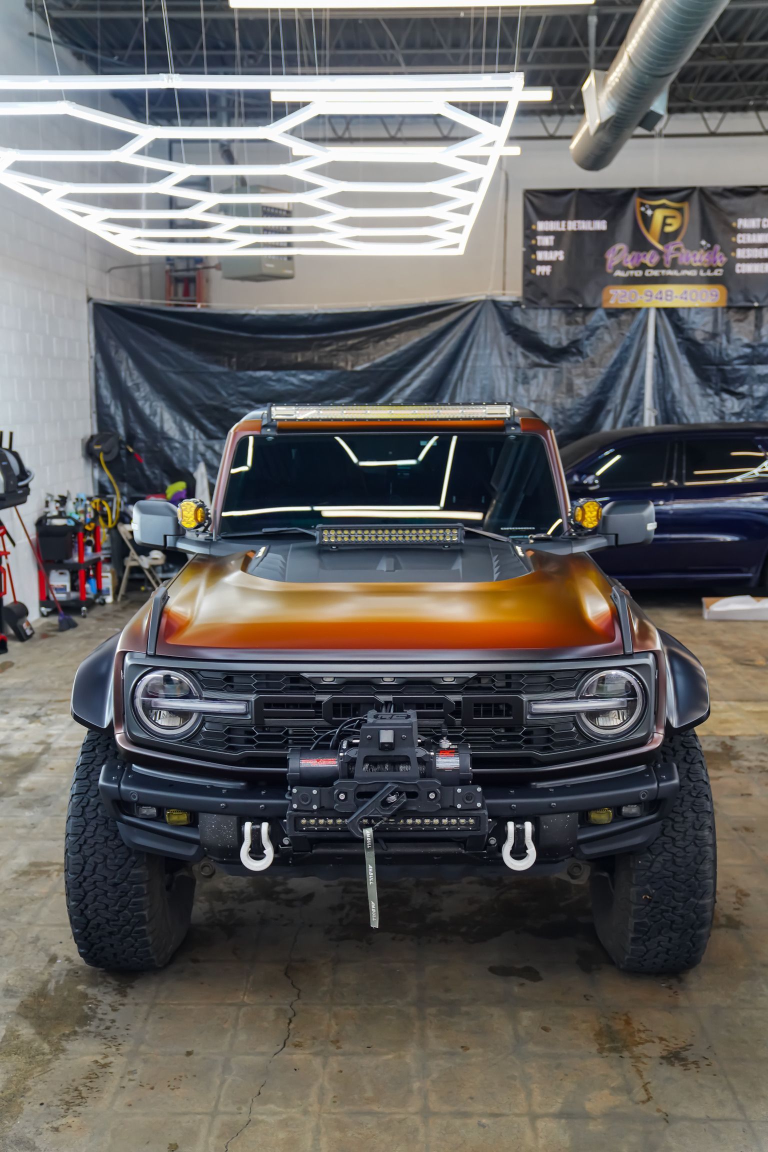 A Ford Bronco with an orange-to-black gradient paint job, off-road tires, and a winch parked inside a professional shop.