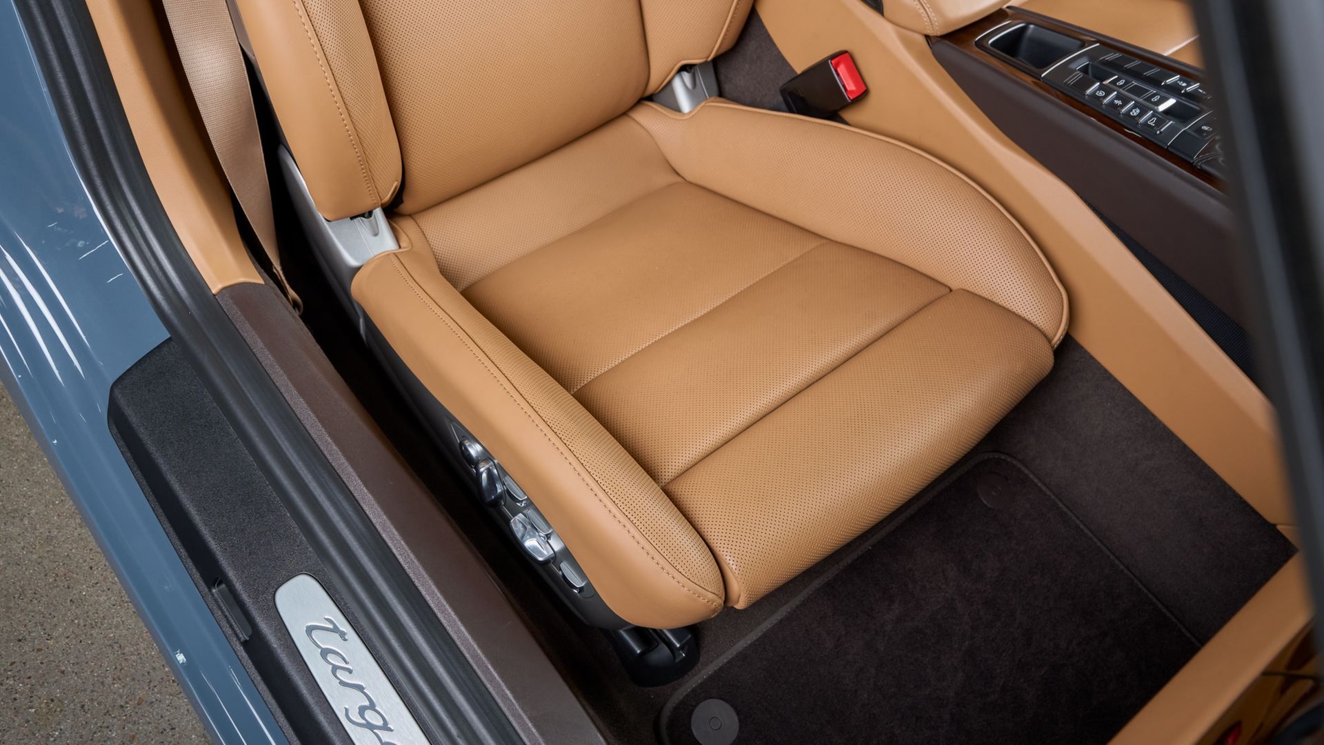 A person kneels to apply a protective film to the front bumper of a blue sports car in an auto shop.