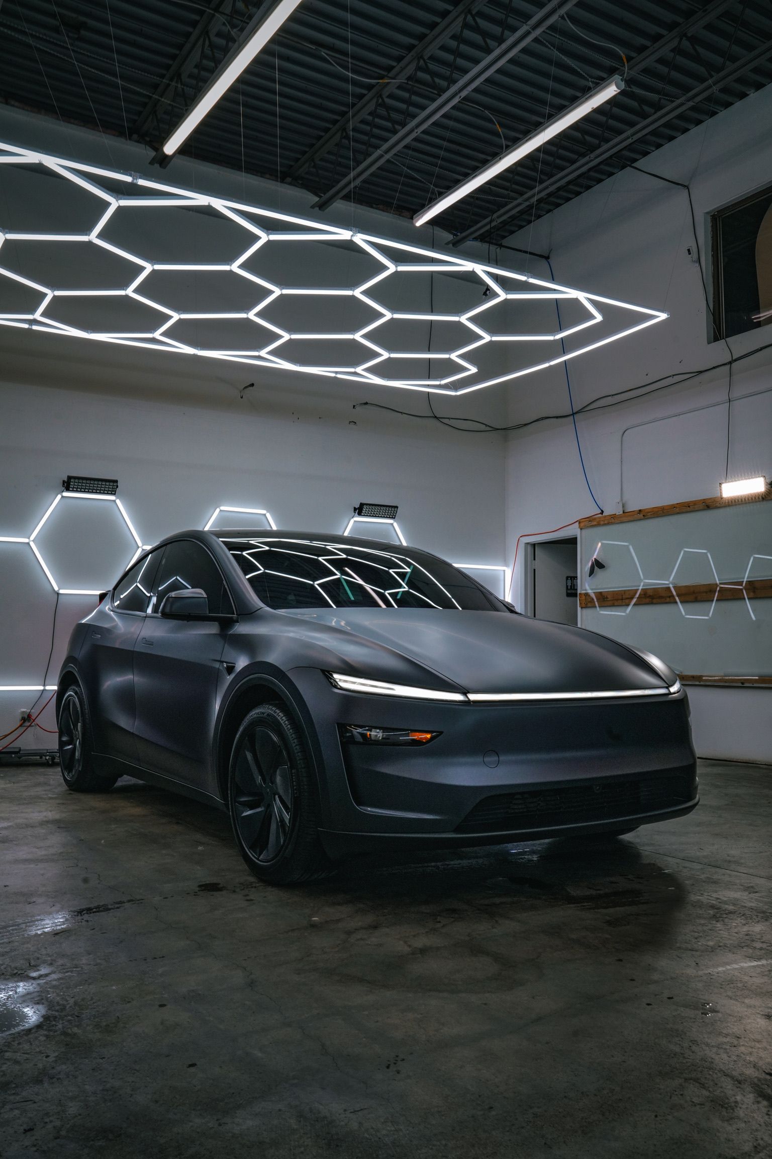 A matte dark grey electric SUV parked in a garage with hexagonal overhead LED lighting.