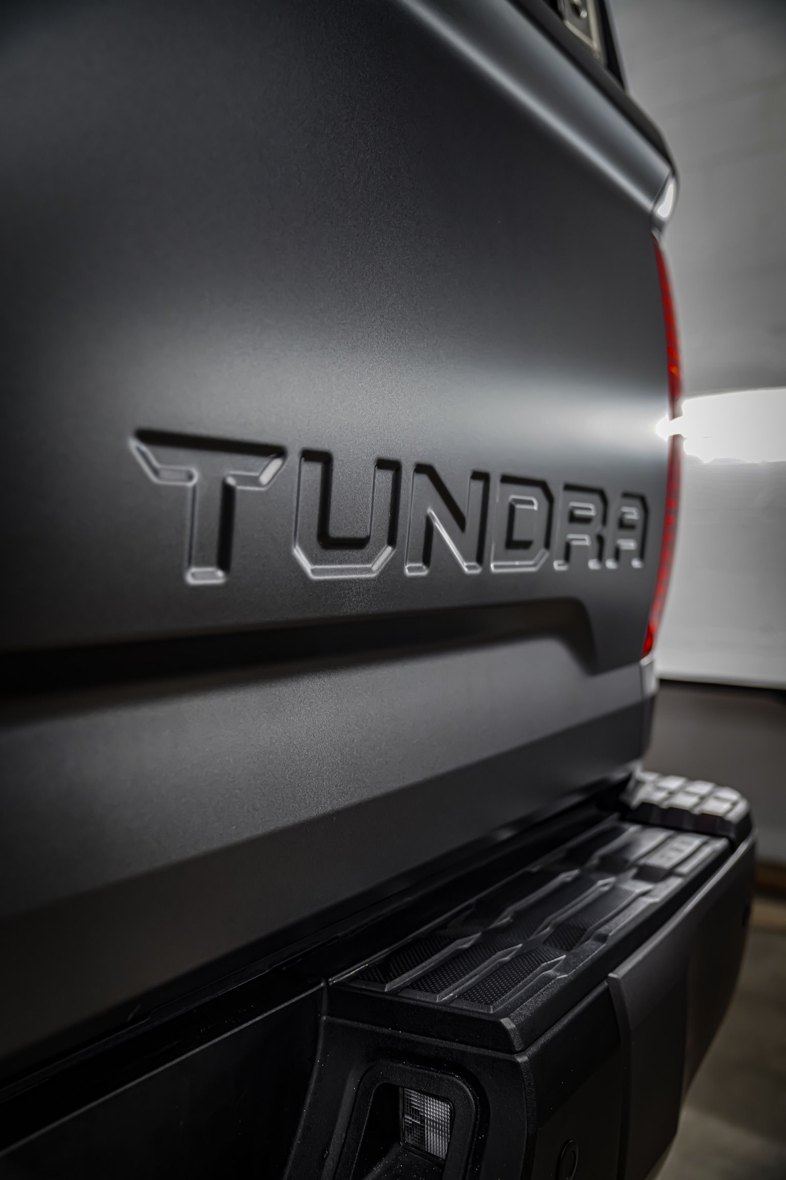 A person kneels to apply a protective film to the front bumper of a blue sports car in an auto shop.