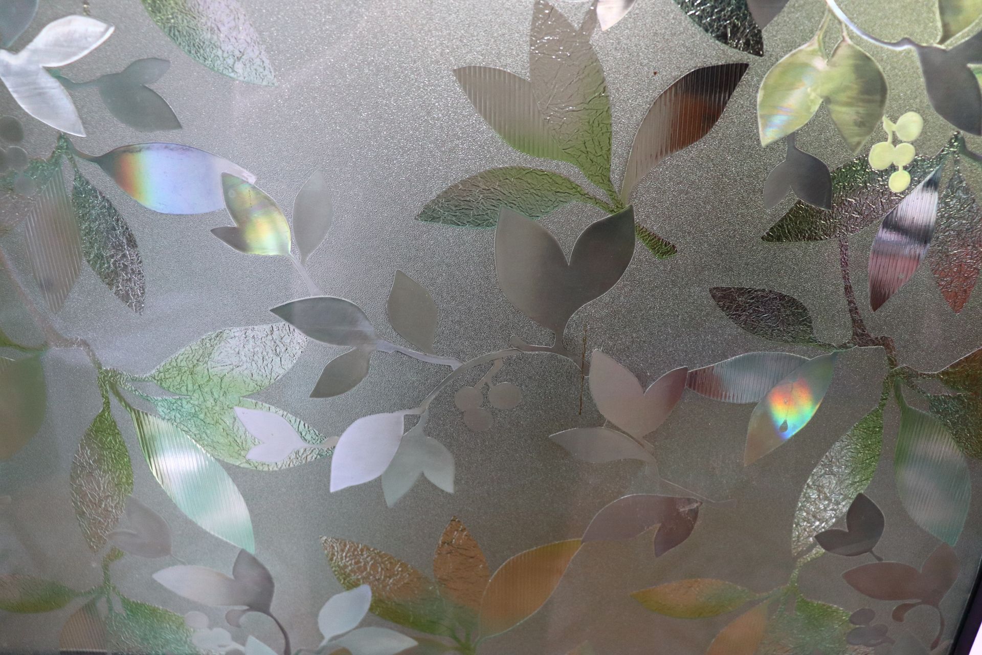 A person kneels to apply a protective film to the front bumper of a blue sports car in an auto shop.