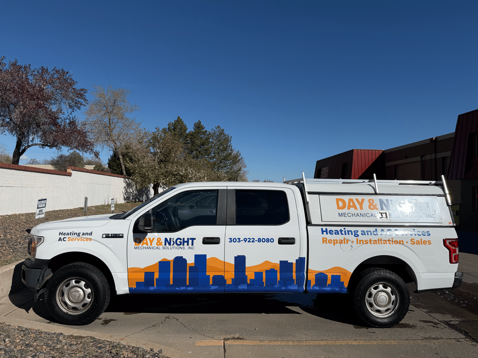 A white P.B. Roche pickup truck is parked in a parking lot on a sunny day with buildings in the background.