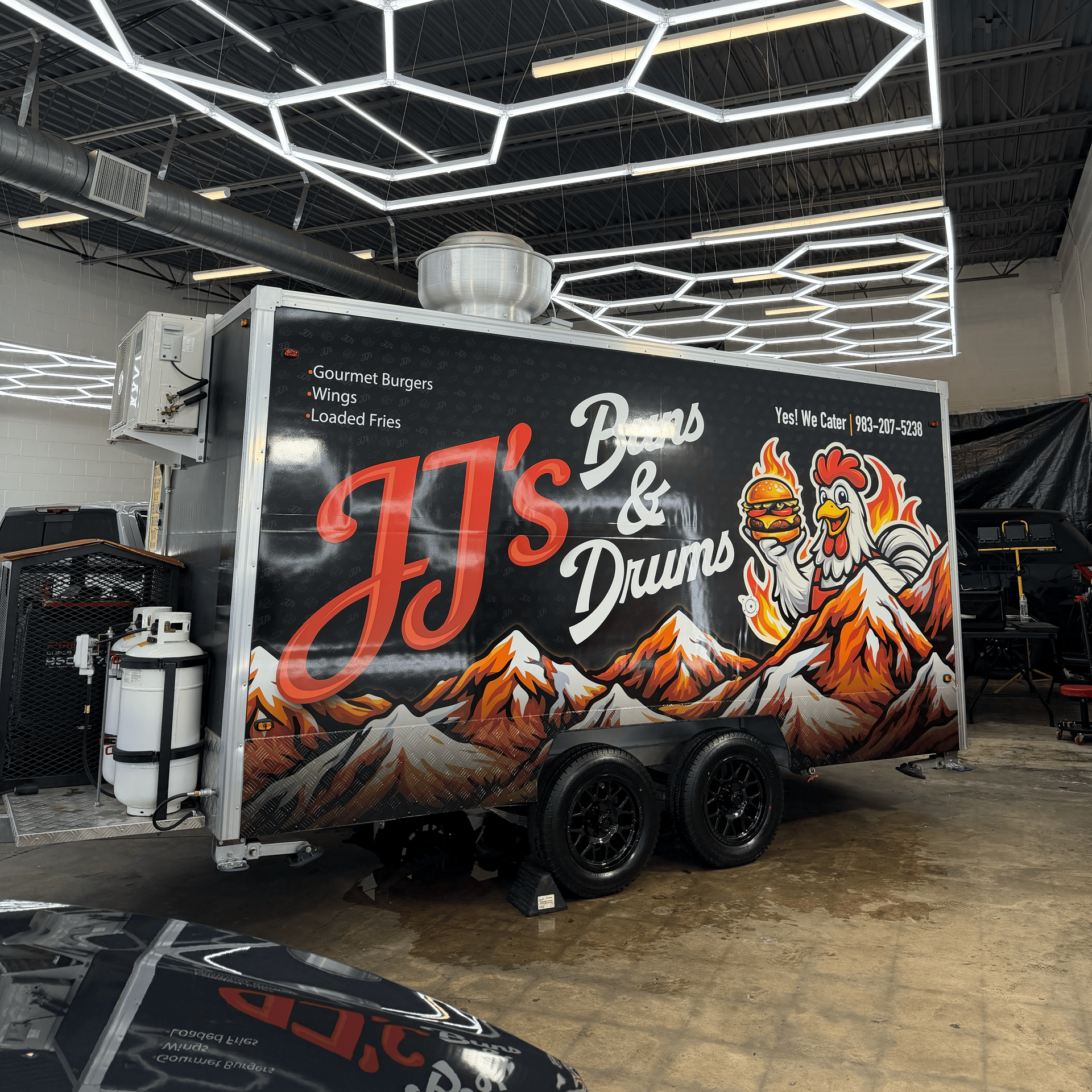 A matte black Tesla Cybertruck parked on a paved lot in front of a building with red metal siding.