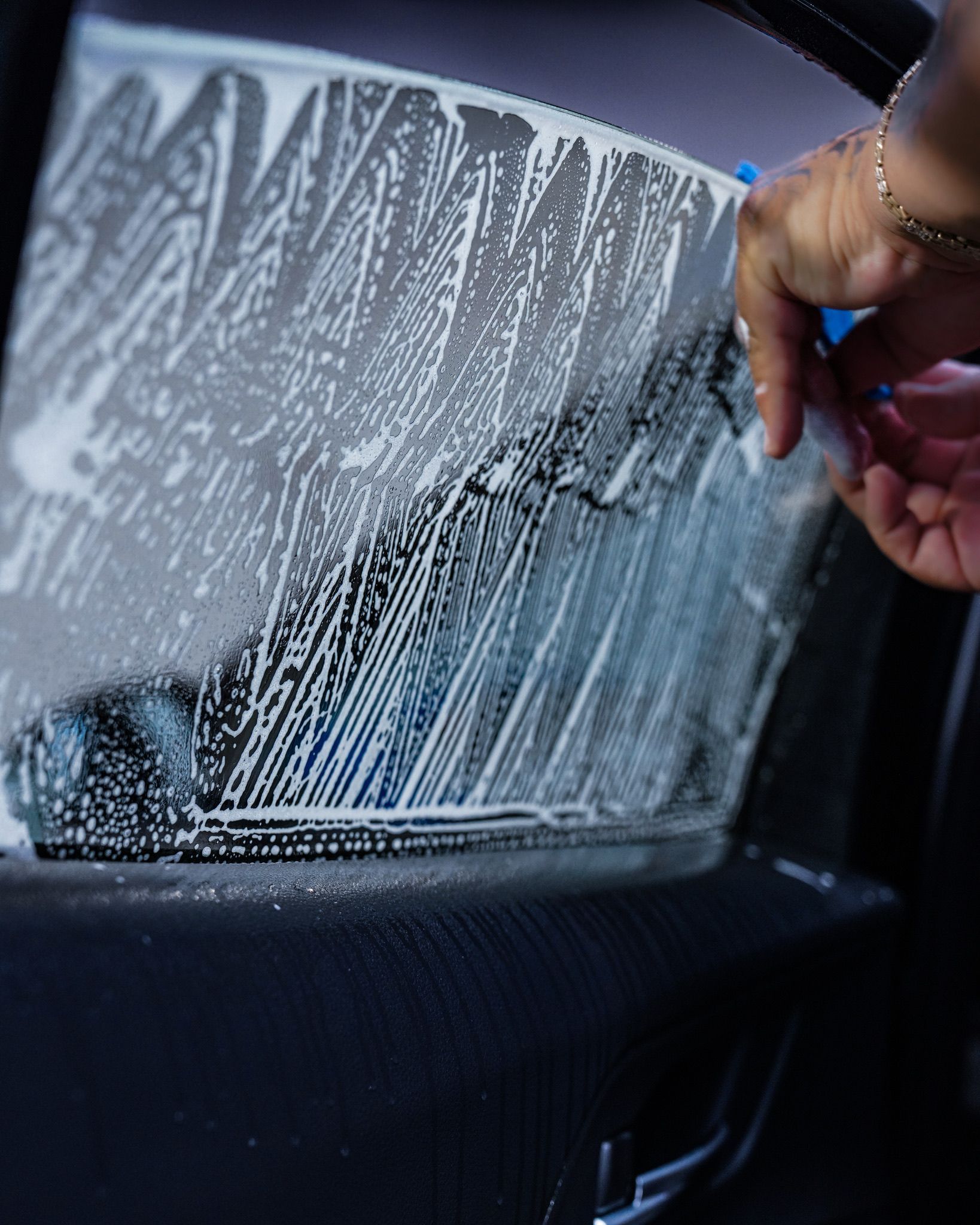 A close-up of a person's hand applying a soapy cleaning solution to a car window before installing window tint.