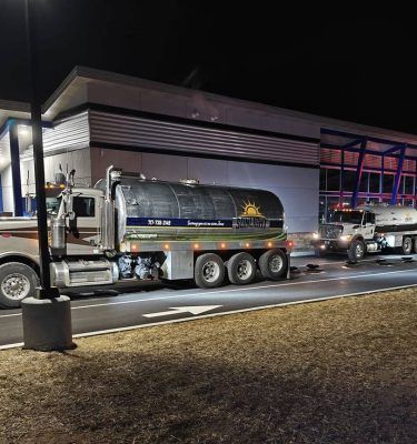 Two tanker trucks parked at night outside a lit industrial building