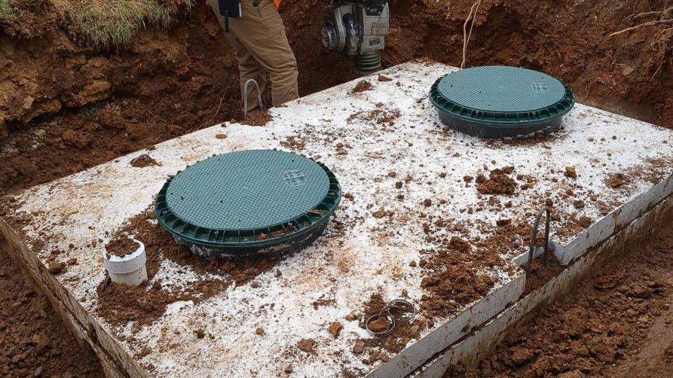 Two green septic tank lids on a concrete slab in a dirt excavation area