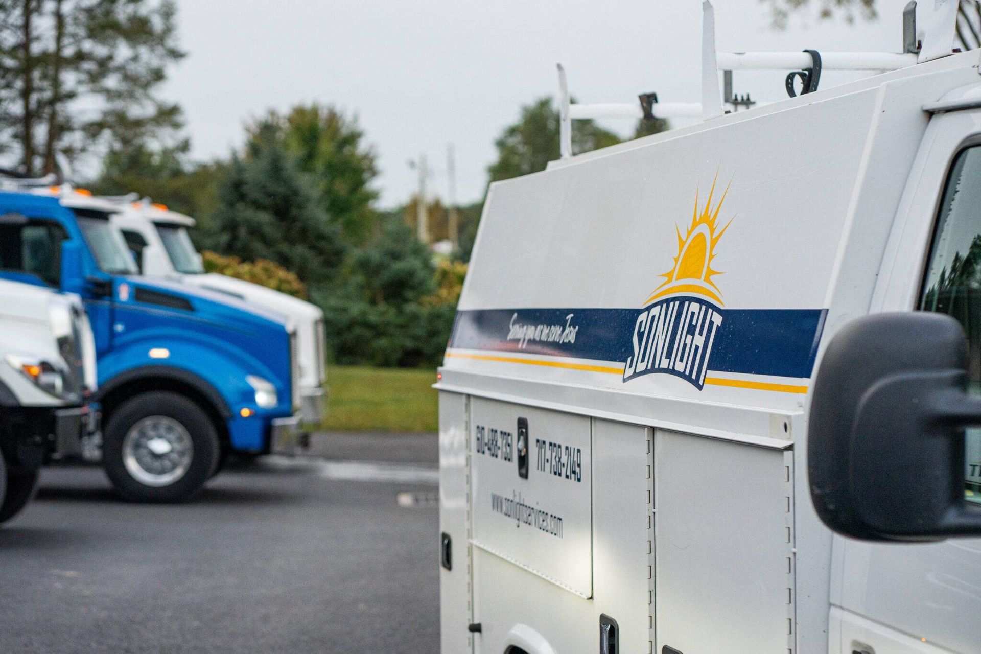 White utility trucks parked outdoors, including a blue truck and a white truck with a sun logo.
