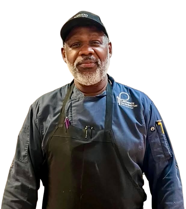 Chef wearing a black apron and cap with a logo, smiling, indoors.