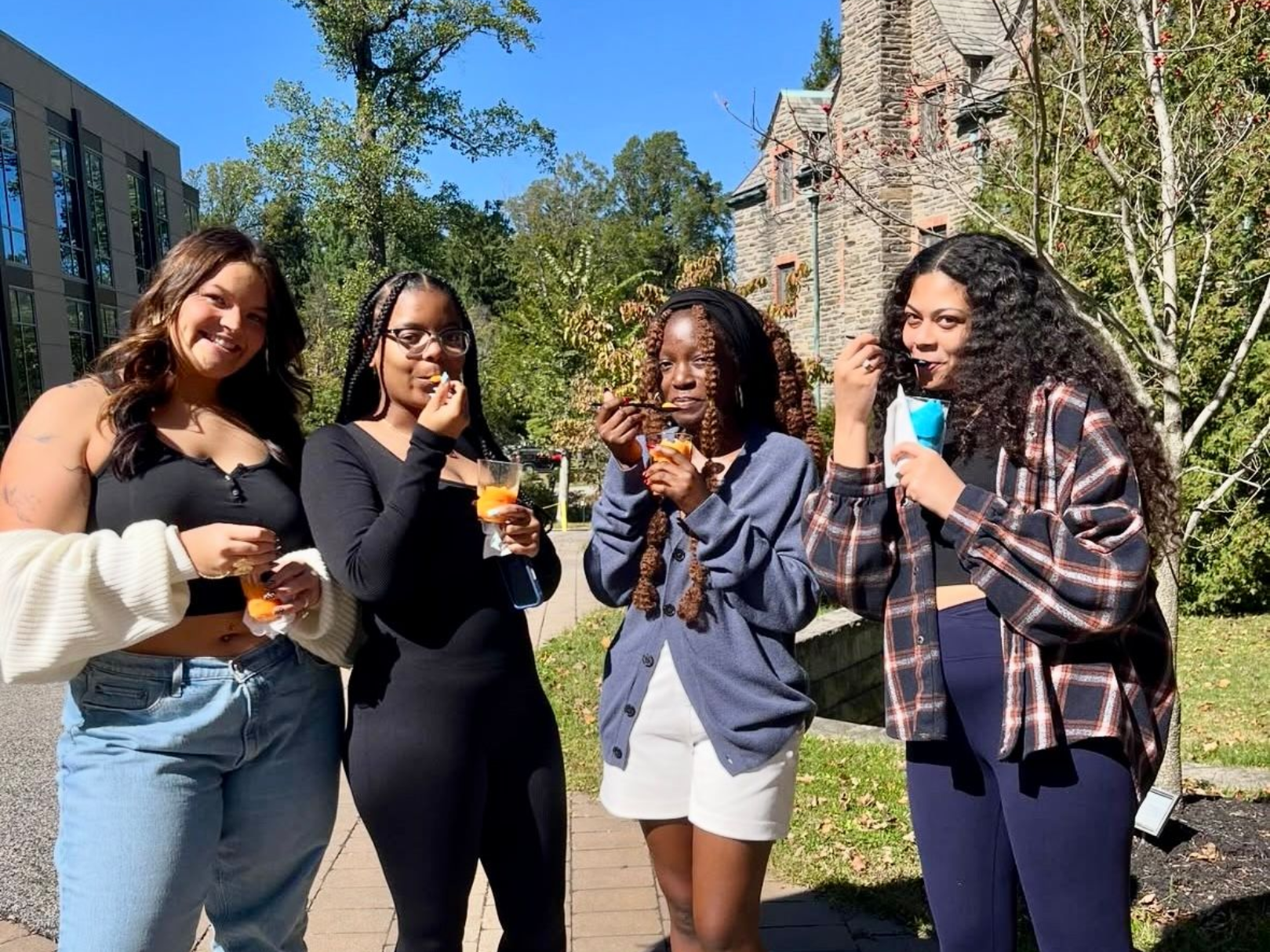 Four people eating treats outdoors near a stone building.