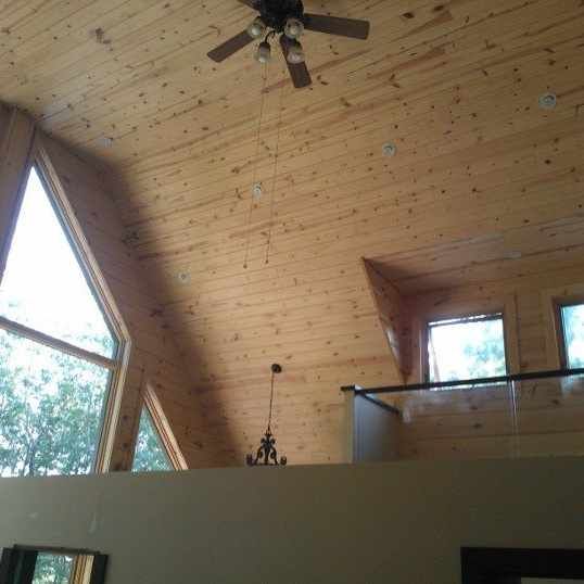 A vaulted wood-paneled ceiling with a ceiling fan, hanging light fixture, and large triangular and rectangular windows.